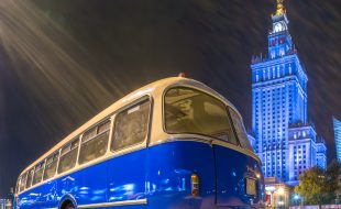 zdjęcie przedstawia biało-niebieski autobus ogórek na tle podświetlonego na niebiesko Pałacu Kultury i Nauki